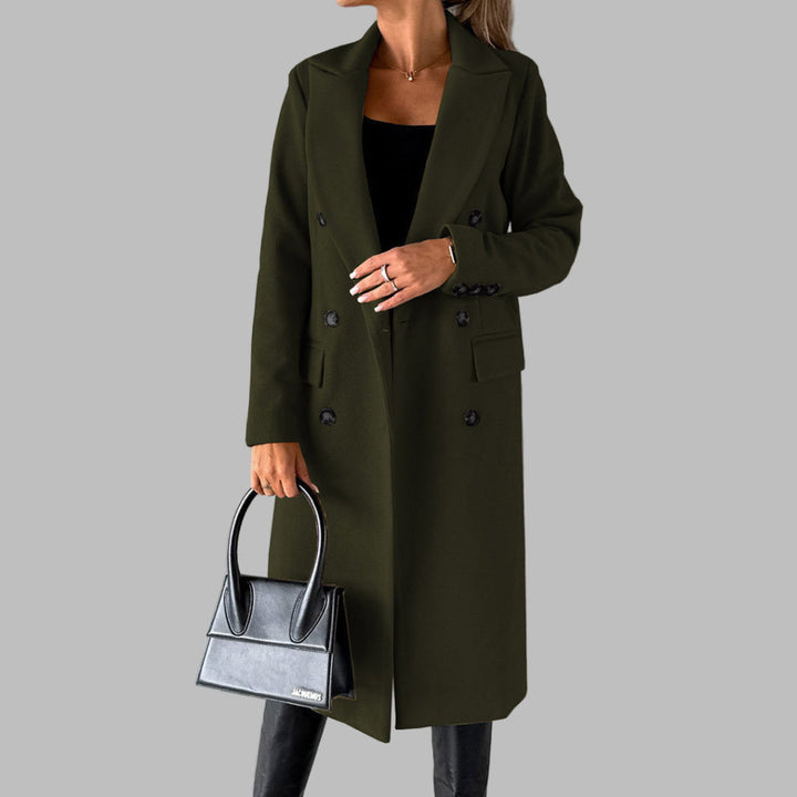 Vrouw in olijfgroene winterjas met dubbele knopen, zwarte handtas y zwarte laarzen tegen een grijze achtergrond. Stijlvolle damesmode.