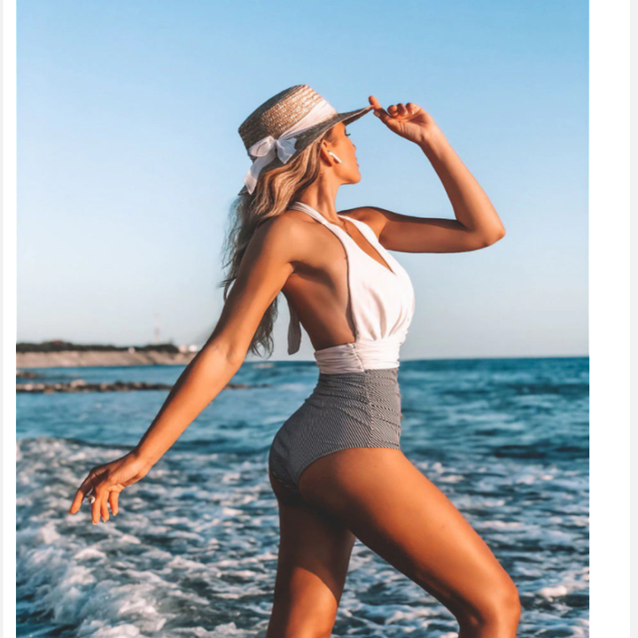 Frau im weißen Badeanzug mit Strohhut am Strand, Sommermode, Meereshintergrund.
